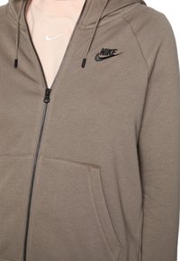 Brun Nike zip-up huvtröja med dragsko, med en svart logotyp, framfickor och en slät, mjuk textur.