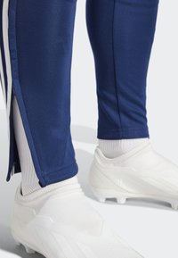 Marineblauwe sportbroeken hebben een taps toelopend ontwerp, witte ritsen bij de enkels en worden gecombineerd met witte voetbalschoenen en gestructureerde witte sokken.