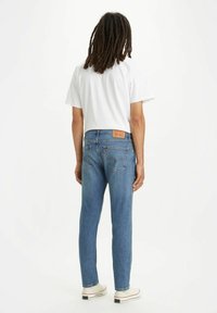 Vaqueros de mezclilla azul claro con un corte recto, diseño de cinco bolsillos y parche de cuero en la cinturilla. Combinados con una camiseta blanca lisa.