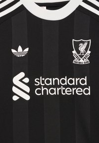 Črna in temno siva črtasta nogometna majica z belim ovratnikom, grb Liverpool FC, logotip Adidas in logotip sponzorja Standard Chartered.