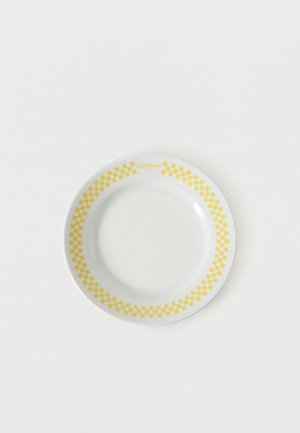 Assiette en céramique blanche avec un motif à carreaux jaunes autour du bord, centrée sur un fond blanc uni.
