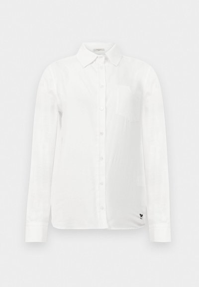 Vit långärmad skjorta med knapp-ned krage, en enda bröstficka och subtilt texturerad tyg. Har detaljer med svart broderad logga.