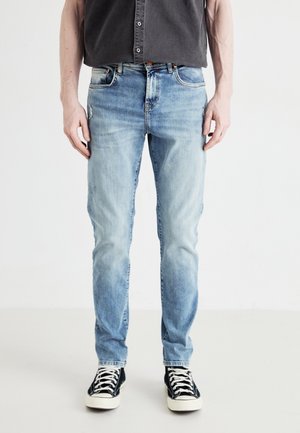 Light blue denim jeans with a slim fit, featuring front pockets and subtle fading. Paired with black and white sneakers.