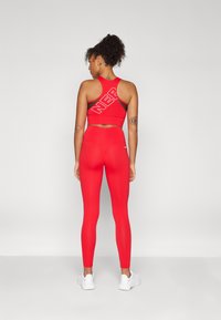 Cropped top sportivo rosso con stampa "NEP" e accenti neri, abbinato a leggings rossi a vita alta. Entrambi realizzati in tessuto elasticizzato, indossati con sneakers bianche.