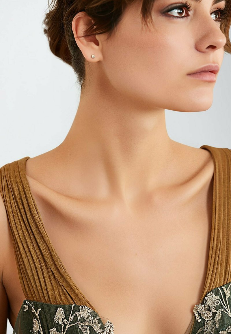 Vestido bordado en verde profundo con un escote plisado dorado. Presenta una capa transparente con patrones florales. Pendientes de botón simples visibles.