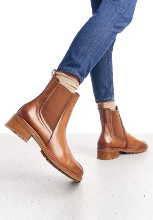 Bottes de cheville en cuir marron avec des panneaux élastiques sur les côtés, bout arrondi et un talon en bois épais. La semelle présente un motif de grip texturé.