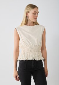 Top sans manches de couleur crème avec une taille froncée et un ourlet noir à volants, fabriqué en tissu léger, doté d'un col rond et d'une texture lisse.