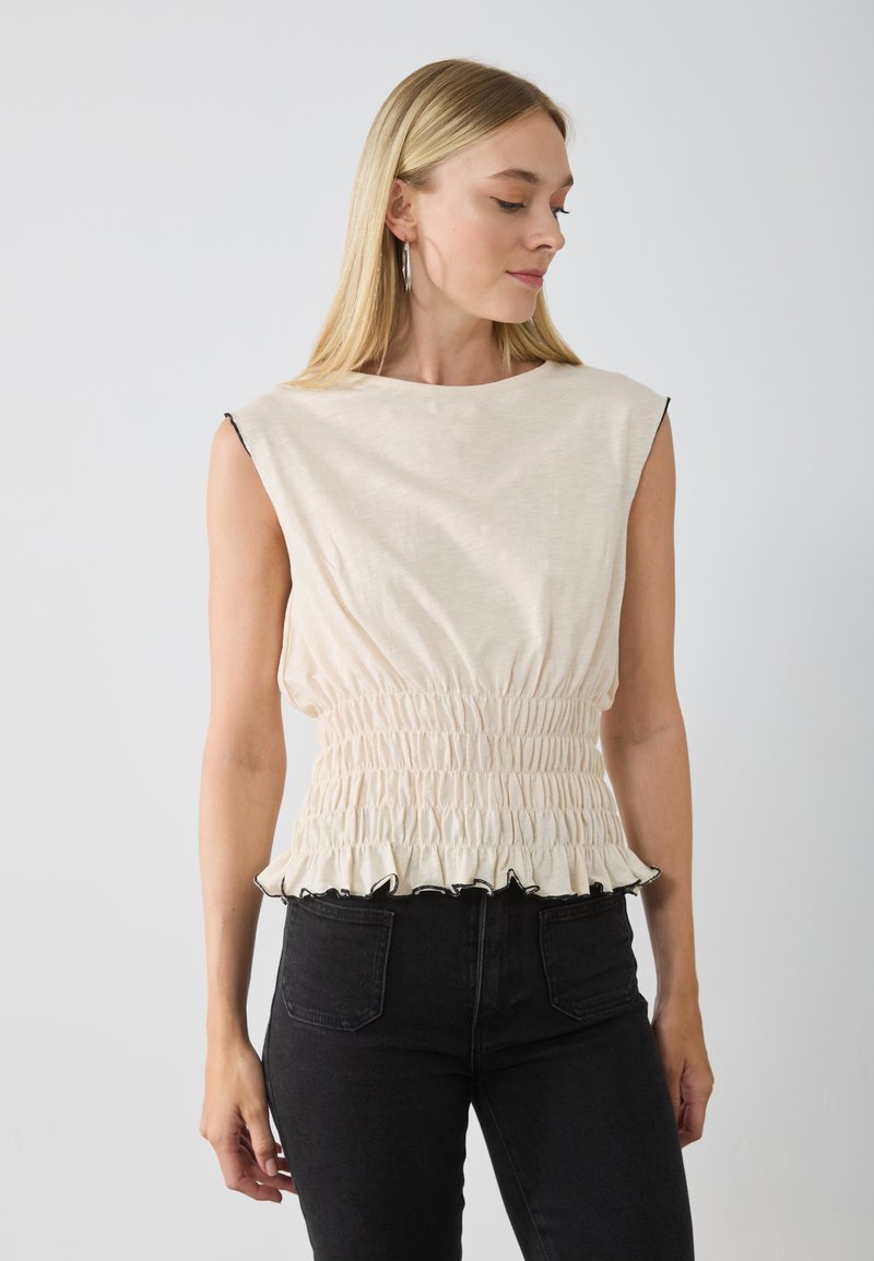 Top sans manches de couleur crème avec une taille froncée et un ourlet noir à volants, fabriqué en tissu léger, doté d'un col rond et d'une texture lisse.