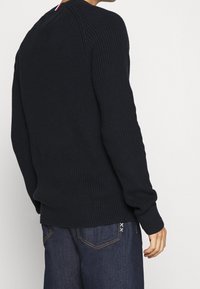 Pull bleu marine en maille avec une texture côtelée, doté de manches raglan et d'un large poignet. Design simple, sans motifs ni accents visibles.