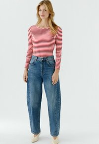 Rood-wit gestreept top met lange mouwen, gecombineerd met hooggetailleerde, loszittende blauwe spijkerbroek. Model draagt lichtgekleurde schoenen met puntige neus.