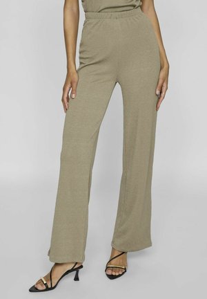 Olijfgroene, wijd gesneden broek van een gestructureerde stof met een elastische tailleband, gecombineerd met zwarte sandalen met bandjes.