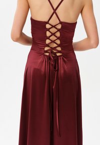 Vínová šaty s saténovým povrchem, s designem na kříž na zádech, nastavitelným stahováním v pase a hladkou texturou.
