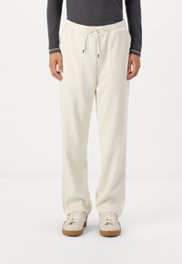 Krémfarvede ribbede sweatpants med elastisk talje og snøre. Har to frontlommer. Sammen med hvide sneakers.