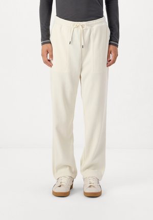 Krémfarvede ribbede sweatpants med elastisk talje og snøre. Har to frontlommer. Sammen med hvide sneakers.