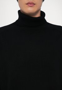 Čierny rolák vyrobený z mäkkého, štruktúrovaného pleteného materiálu, s priliehavým strihom a vysokým golierom. Jednoduchý a univerzálny štýl.