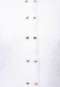 Άσπρη χνουδωτή ζακέτα με μεταλλικά κουμπιά σε σχήμα καρδιάς τοποθετημένα σε σειρά μπροστά, προσφέροντας απαλότητα και ζεστή εμφάνιση.