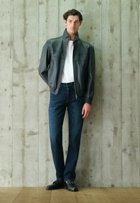 Chaqueta de cuero negra con cremallera, camiseta blanca, vaqueros azul oscuro, zapatos negros. Textura suave, corte ajustado, con bolsillos para las manos y cuello con puntas.