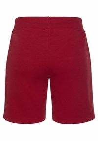 Red cotton shorts featuring an elastic waistband, mid-thigh length, and smooth texture. No additional patterns or accents visible.