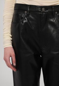 Schwarze Lederhosen mit glatter Oberfläche, ausgestattet mit Fronttaschen, einem Knopfverschluss und subtilen Steppdetails.