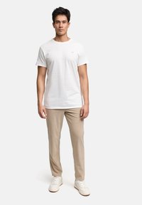 T-shirt bianca in cotone, maniche corte, abbinata a pantaloni beige a coste e sneakers bianche. Design minimalista con un sottile dettaglio del logo sulla maglietta.