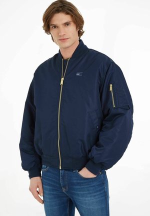Chaqueta bomber de marina con cremallera dorada, puños acanalados y parche con logo. Fabricada en una tela suave y liviana con un ajuste ligeramente holgado.