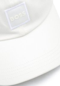Gorra de béisbol blanca de algodón con un parche cuadrado blanco que presenta el logo "BOSS" en relieve. La visera tiene sutilezas en los detalles de costura.