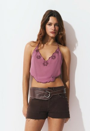 Lavender halter crop top with floral embroidery and scalloped hem, paired with brown denim shorts and a wide studded belt.