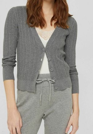 Grijze geribbelde cardigan met een diepe V-hals en zes knoopsluitingen. Lange mouwen, zachte textuur, gecombineerd met een lichtgekleurde top en bijpassende broek.