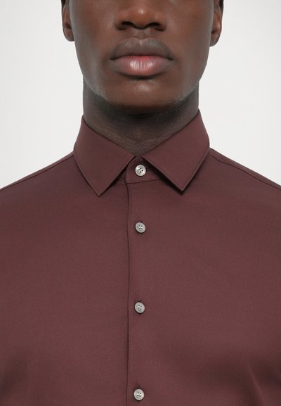 Camisa burdeos de botones con una textura suave, cuello clásico y botones plateados en el frente. Primer plano de la tela y el escote.