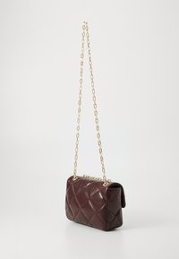 Sac à main en cuir bordeaux matelassé avec une bandoulière en chaîne dorée. Présente une forme rectangulaire et un léger éclat, avec des détails en motif de diamants.