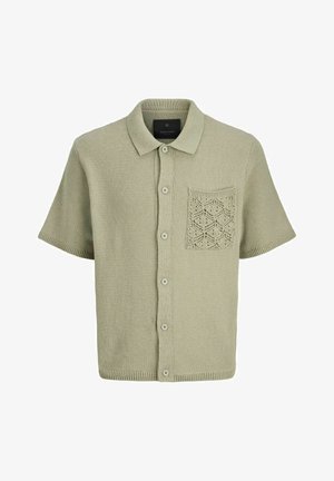 Kortermet skjorte med knapp i lysegrønn strikket stoff. Har en teksturert lomme med et geometrisk mønster. Klassisk krage og fem knapper.