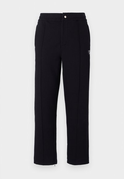 Black sweatpants with a tailored fit, featuring side seams, a zippered hem, and a metal button closure at the waist. Subtle branding detail.