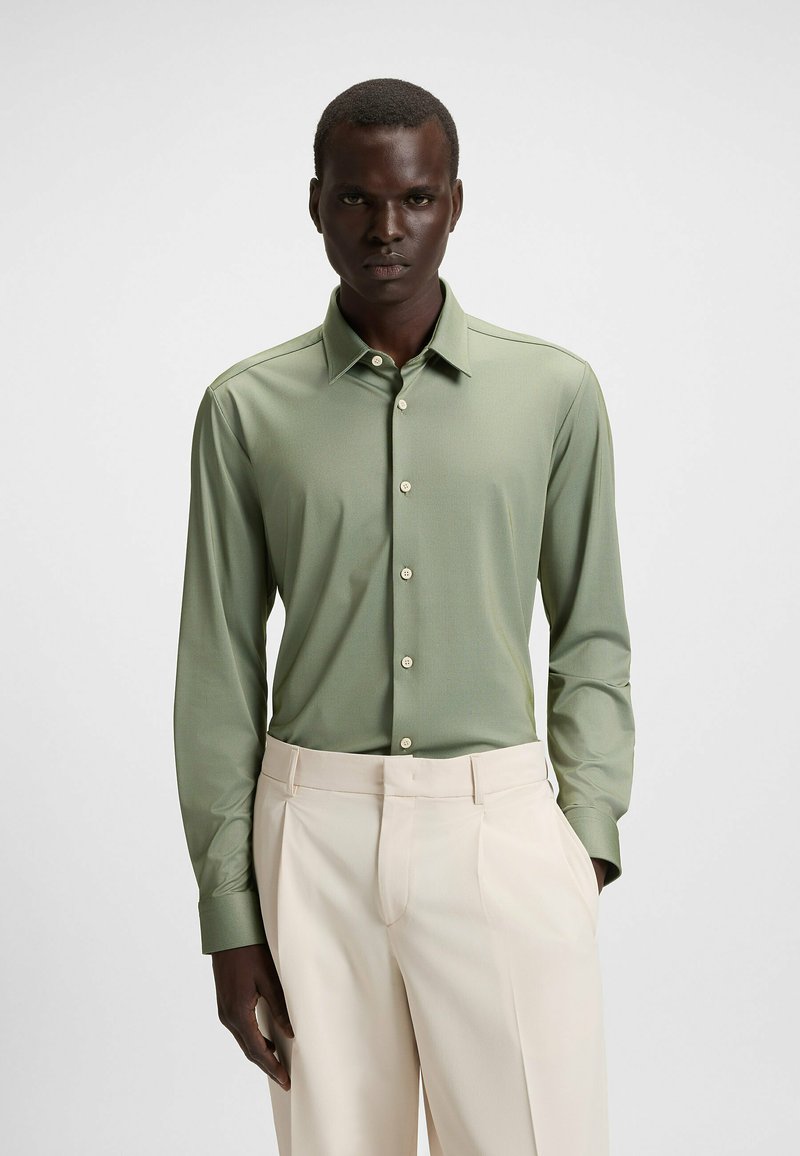 Groene overhemd met lange mouwen, een puntige kraag, voorknopsluiting en een gladde textuur, gecombineerd met lichtbeige broek.