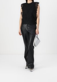 Top en dentelle noire avec des bords festonnés, associé à un pantalon en cuir noir taille haute. Tenant une pochette métallisée argentée, accompagné de chaussures argentées à talons pointus.