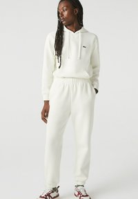 Vitt hoodie och matchande sweatpants i ribbad textur. Har en liten grön logotyp på bröstet och elastiska muddar vid ankle.