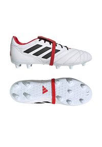 Scarpe da calcio bianche con strisce nere, dettagli rossi e una suola testurizzata con tacchetti per trazione. Include una fascia rossa sopra i lacci.