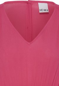 Blouse rose sans manches avec col en V et couture visible au dos, avec une étiquette blanche portant le texte "ICHI".