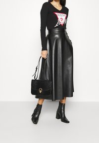 Atasan lengan panjang hitam dengan cetakan grafis, rok kulit hitam berpinggang tinggi, sepatu bot pergelangan kaki bertumit hitam, dan tas tangan hitam dengan embossing krokodil.