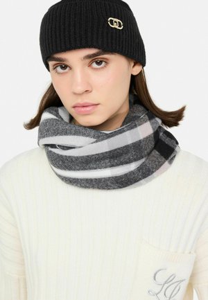 Beanie nero a coste con un logo accentato dorato; sciarpa circolare a strisce grigie e bianche; texture morbida; indossato sopra un maglione crema.