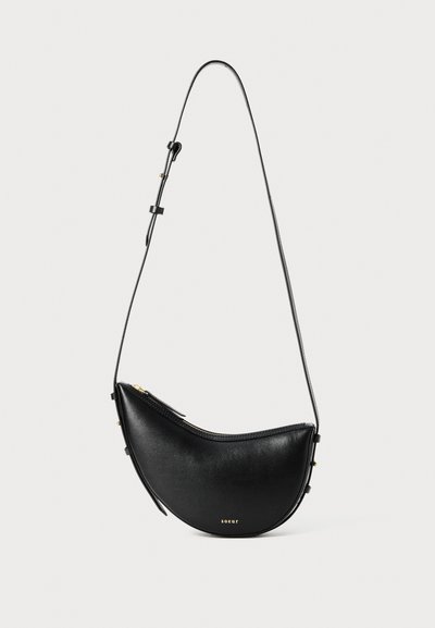 Sac à main en cuir noir avec une forme courbée et une seule sangle ajustable. Dispose d'une fermeture éclair et d'un matériel minimal en doré.