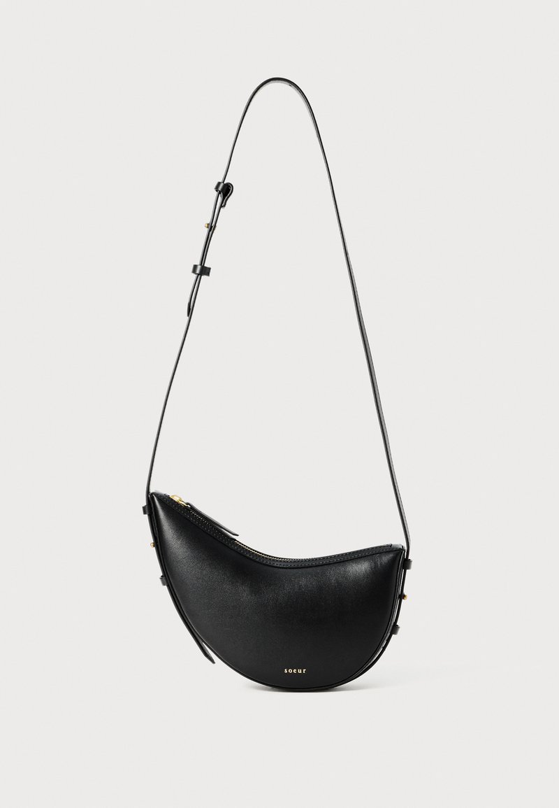 Černá kožená kabelka s zakřiveným tvarem a jedním nastavitelným popruhem. Obsahuje zipové uzavření a minimální zlaté kovové detaily.