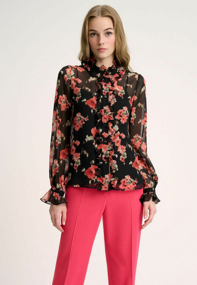 Blusa negra transparente con estampado floral en rojo y rosa; cuello y puños con volantes; cierre frontal con botones; combinada con pantalones rosa.