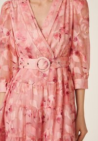 Vestido cruzado rosa con estampado floral, mangas abullonadas de tres cuartos y cinturón a juego con hebilla redonda en la cintura.