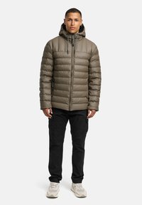 Pufferjakke i olivengrøn, quiltet design med hætte, med frontlynlås og sidelommer, parret med sorte cargo-bukser og sneakers.