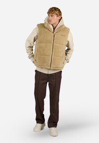 Viltīgs, beisīgs veste ar augstu apkakli un rāvējslēdzēju priekšā. Tam ir kvadrātveida pildījums, sānu kabatas un logo kreisajā krūtīs. Valkāta virs viegla kapuces krekla.