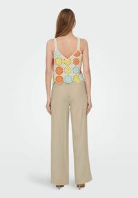 Top de ganchillo con patrones de sol multicolores en naranja, amarillo y azul; combinado con pantalones anchos beige; diseño casual, con escote en la espalda.