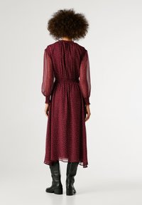 Garšīgs burgundijas kleita ar baltām punktiņām, caurspīdīgām garām piedurknēm, smilšu viduklis, plūstoša svārku daļa, apvienots ar melniem zābakiem līdz celim.