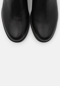 Chaussures en cuir noir à bouts arrondis vues de dessus sur un fond clair.