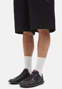 Black leather shoes with elastic laces, paired with white crew socks. Worn with knee-length black shorts, showcasing a casual look.