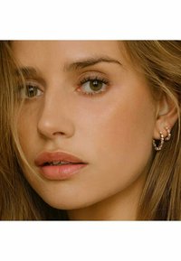 Orecchini ad anello color oro decorati con pietre trasparenti e brillanti; finitura liscia; vista ravvicinata di un modello che li indossa con capelli lunghi e mossi.